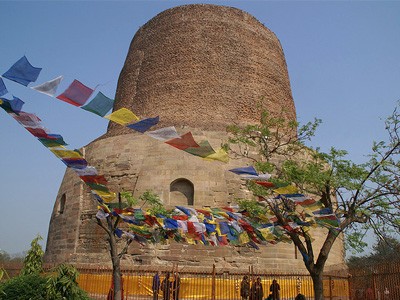 The Dhamek Stupa under clear blue sky with Tibetan prayer flags in front.