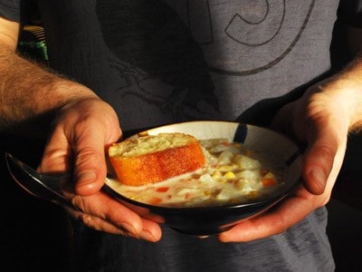 A man holding a bowl of corn soup with a small piece of bread.