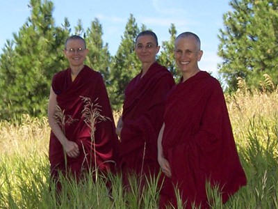 Venerables Tarpa, Saldon, and Chodron standing outside in the lower Abbey meadow.