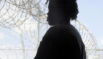 Young person behind a prison fence.