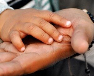 The hands of a child and parent, touching.