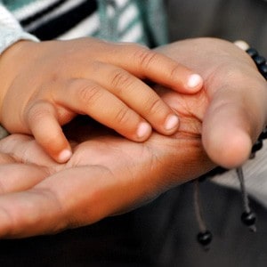 The hands of a child and parent, touching.
