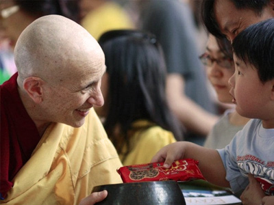 Venerable Chodron, smiling, receiving alms from a young boy.
