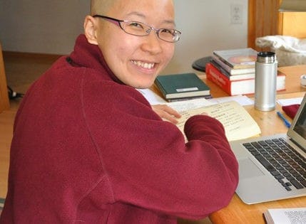enerable Damcho smiling, with a book and laptop.