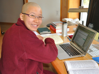Venerable Damcho smiling, with a book and laptop.
