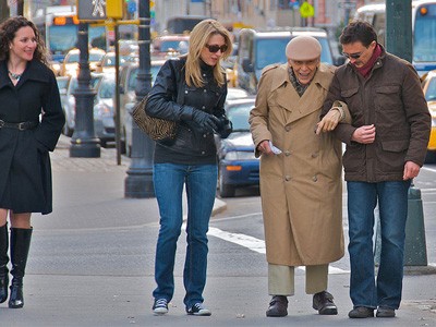 Young man helping elderly man walk.