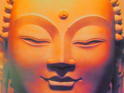 Close-up of orange-colored face of smiling Buddha.