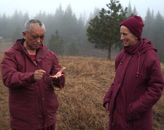 Le Vénérable Chodron et Lama Zopa Rinpoché, debout à l'extérieur, en conversation.