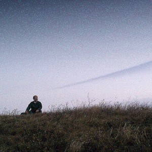 Mężczyzna siedzący na zewnątrz w polu pod bezchmurnym niebem o zmierzchu.