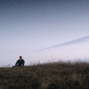 Man sitting outside in field under clear sky at dusk.