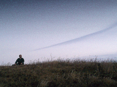 Mężczyzna siedzący na zewnątrz w polu pod bezchmurnym niebem o zmierzchu.