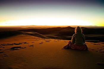 A gril sitting at the summit of the tallest dune at sunset