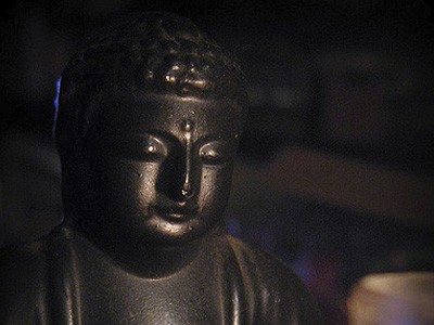 Dark statue of Buddha next to a candle.