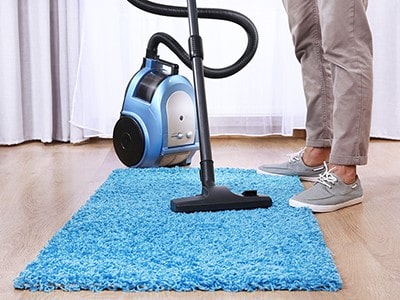 Man vacuuming a blue rug.