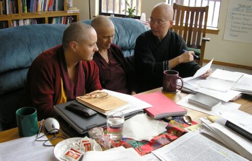 Venerable Jampa Tsedroen, Venerable Thubten Chodron, and Venerable Heng Ching sit at a table filled with research materials.