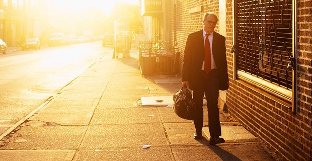 رجل يرتدي بدلة العمل ويحمل حقيبة ، يمشي عند غروب الشمس.