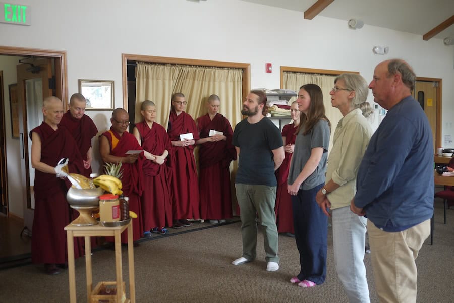 Lay guests read the food offering prayer as monastics listen standing behind an alms bowl with food.