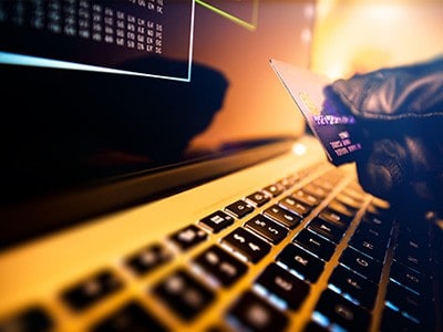 Gloved hand holding credit card at keyboard of computer.
