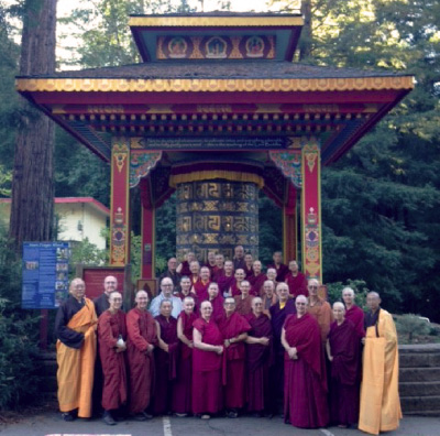 Group of monastics standing in front of large prayer wheel.