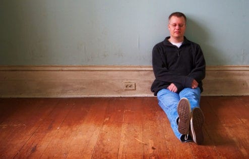 Man sitting on floor, looking sad.