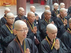 Rows of Buddhist nuns chanting with hands folded.