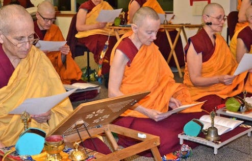 Venerable Chodron and other Abbey monastics sitting on meditation cushions and reading a text.