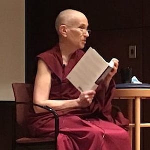 Venerable Chodron sitting in a chair, holding a book and teaching.