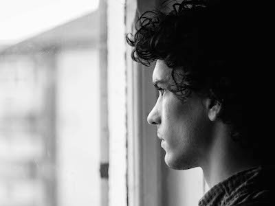 Young man with sad expression looking out a window.
