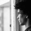 Young man with sad expression looking out a window.