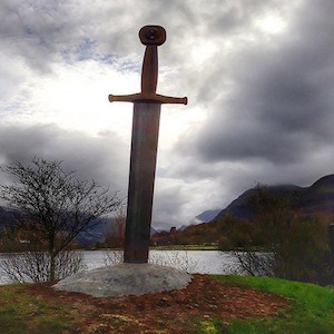 Sværd stikker ud af jorden med dam i baggrunden.