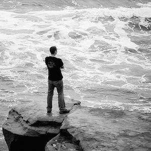 Man standing on a rock looking at the ocean.