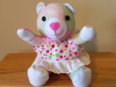 Urso de pelúcia rosa usando um vestido rosa pontilhado.