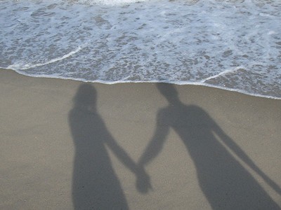 Silueta páru, drželi se za ruce na pláži.