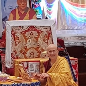 Venerable smiling and teaching in front of large image of His Holiness.