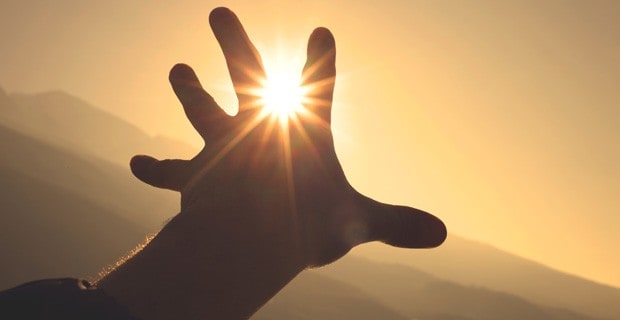 Silhouette of hand reaching out toward the sun.