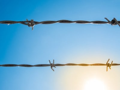 Zwei Stacheldrahtstränge mit blauem Himmel im Hintergrund und Sonnenlicht.