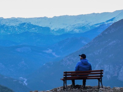 Silhouette of man sitting on bench looking out towards mountain range.