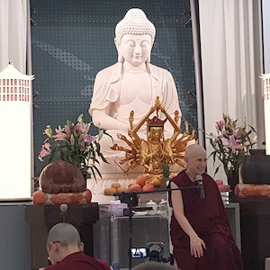 Venerable sitting in front of large Buddha statue, teaching.