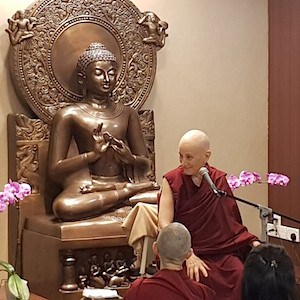 Venerable Chodron in front of a large Buddha statue, smiling while teaching.
