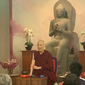 Venerable teaching in front of a large Buddha statue.