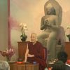 Venerable teaching in front of a large Buddha statue.