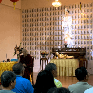 Venerable teaching in front of large Buddha statue.
