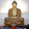Venerable teaching in front of large golden Buddha statue.