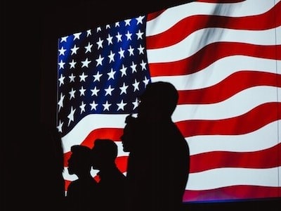 अमेरिकन ध्वजाच्या समोर लोकांचे सिल्हूट.