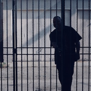 Sylwetka człowieka stojącego za kratami więzienia.