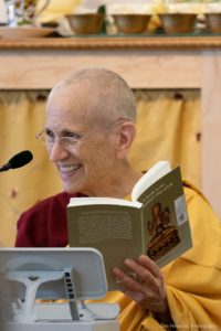 Venerable Chodron holding a book and smiling while teaching.