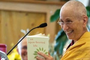 Venerable Chodron smiling while holding a book and teaching.