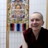 Venerable Sangye Khadro sitting in front of a thangka, smiling.