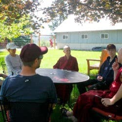 Czcigodny Chodron i uczestnicy Tygodnia Młodych Dorosłych dyskutują o Dharmie przy stole w ogrodzie.