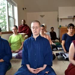 Zakonnicy, świeccy praktykanci i świeccy siedzą w medytacji w opactwie Sravasti.